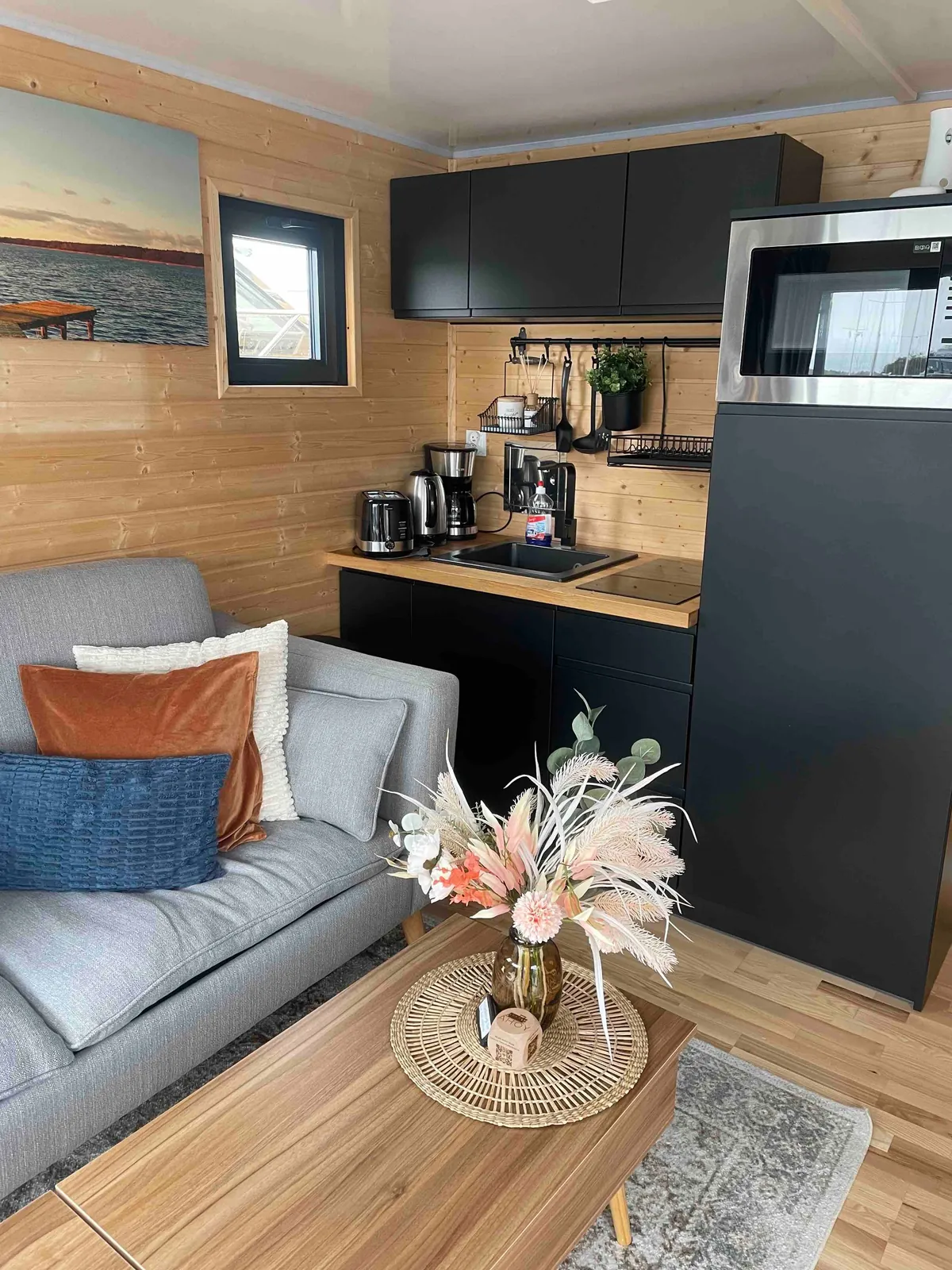 Helle Wohn- und Küchenecke des AHOY Masal mit Sofa, Trockenblumen und warmem Holz